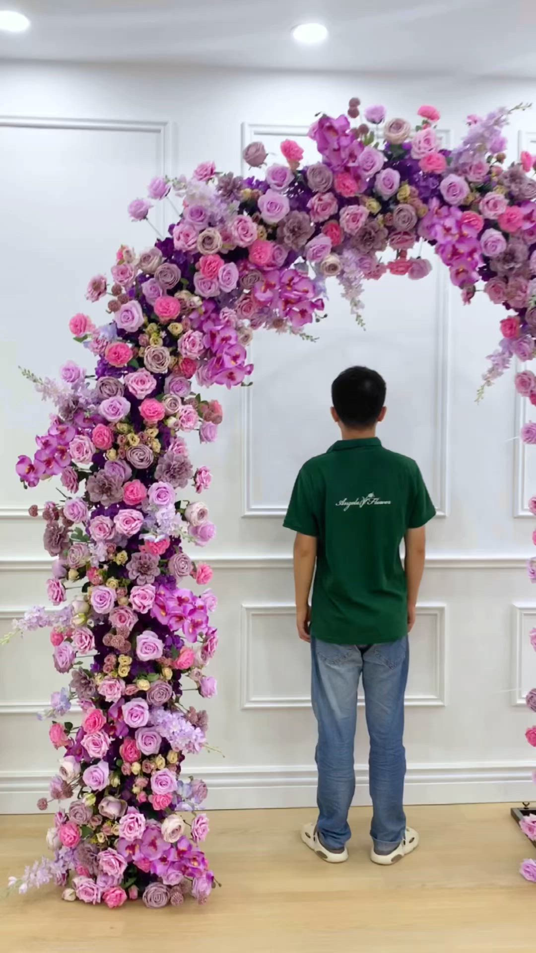 This may contain: a man standing in front of a purple flower arch with lots of flowers on it