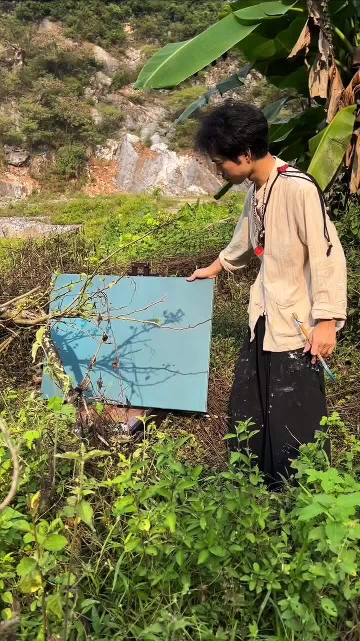 This may contain: a young man standing next to a blue box on top of a lush green hillside