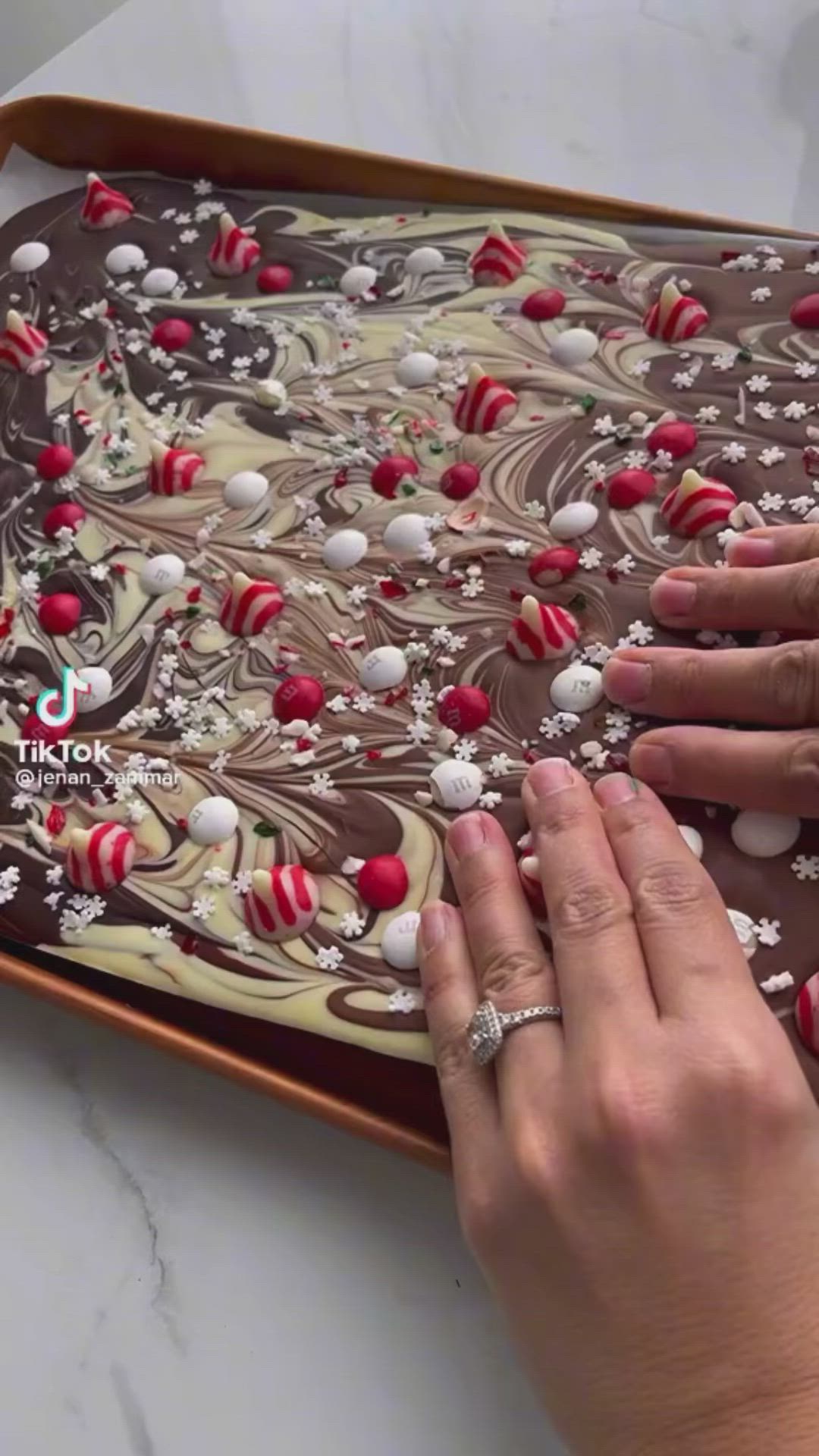 This may contain: two hands are decorating a chocolate cake with red and white decorations on it's surface