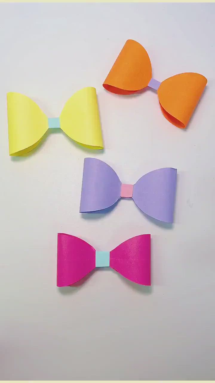 This may contain: three different colored paper bows on a white surface with one pink, one orange and one blue