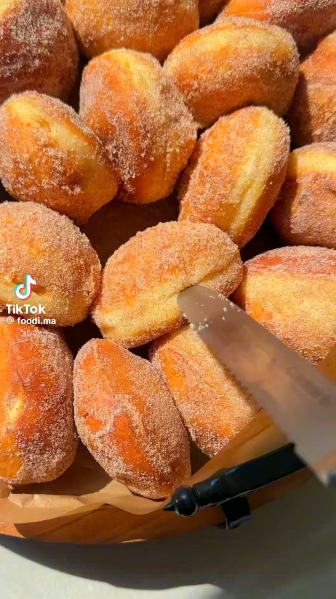 This may contain: sugar coated doughnuts in a basket with a knife