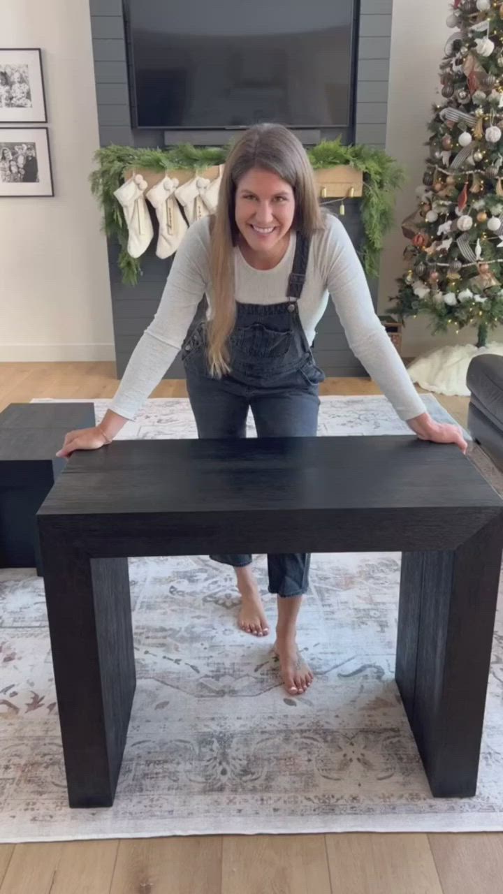 This may contain: a woman sitting at a table in front of a christmas tree with her hands on the top