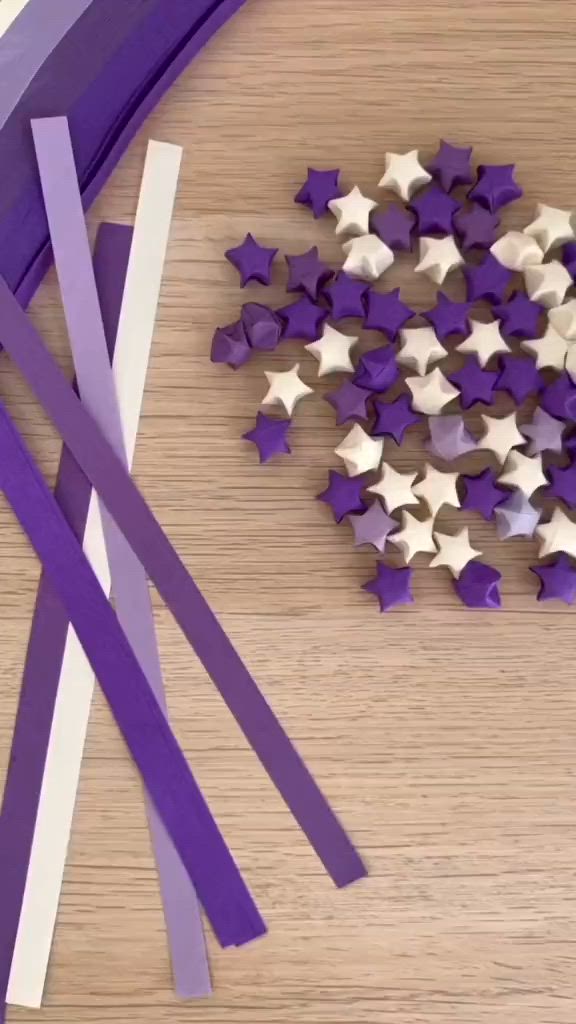 This may contain: two hands holding purple and white paper stars on a wooden table with the words, then you can inflate the star by using your index finger and thumb