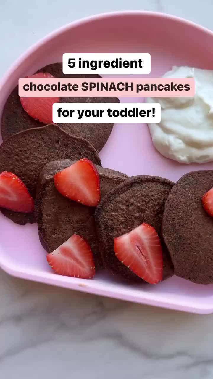 This may contain: a pink plate topped with chocolate pancakes covered in strawberries next to whipped cream and strawberry slices