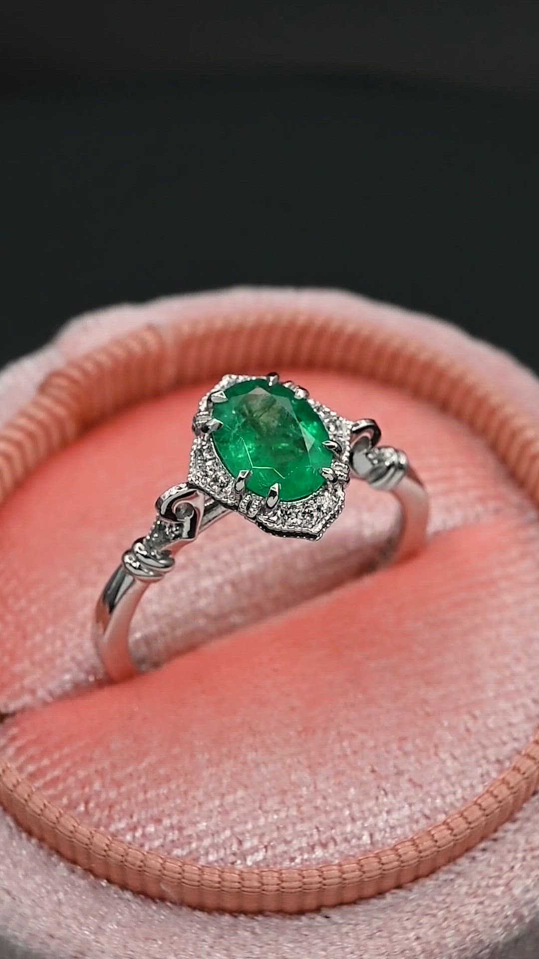 This may contain: an emerald and diamond ring sitting on top of a pink velvet cushion in a box