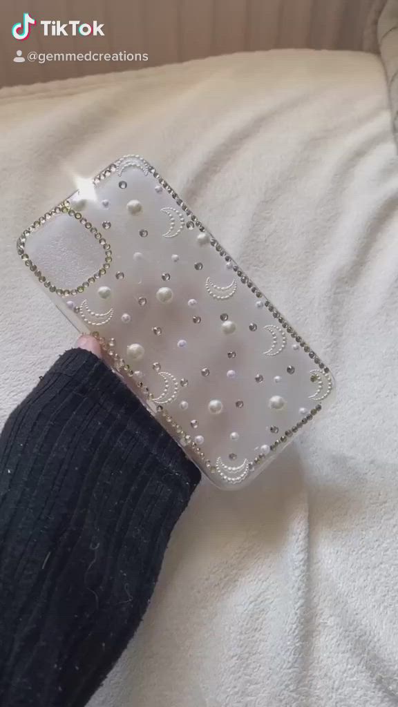 This may contain: a person's hand holding a cell phone case with pearls and diamonds on it