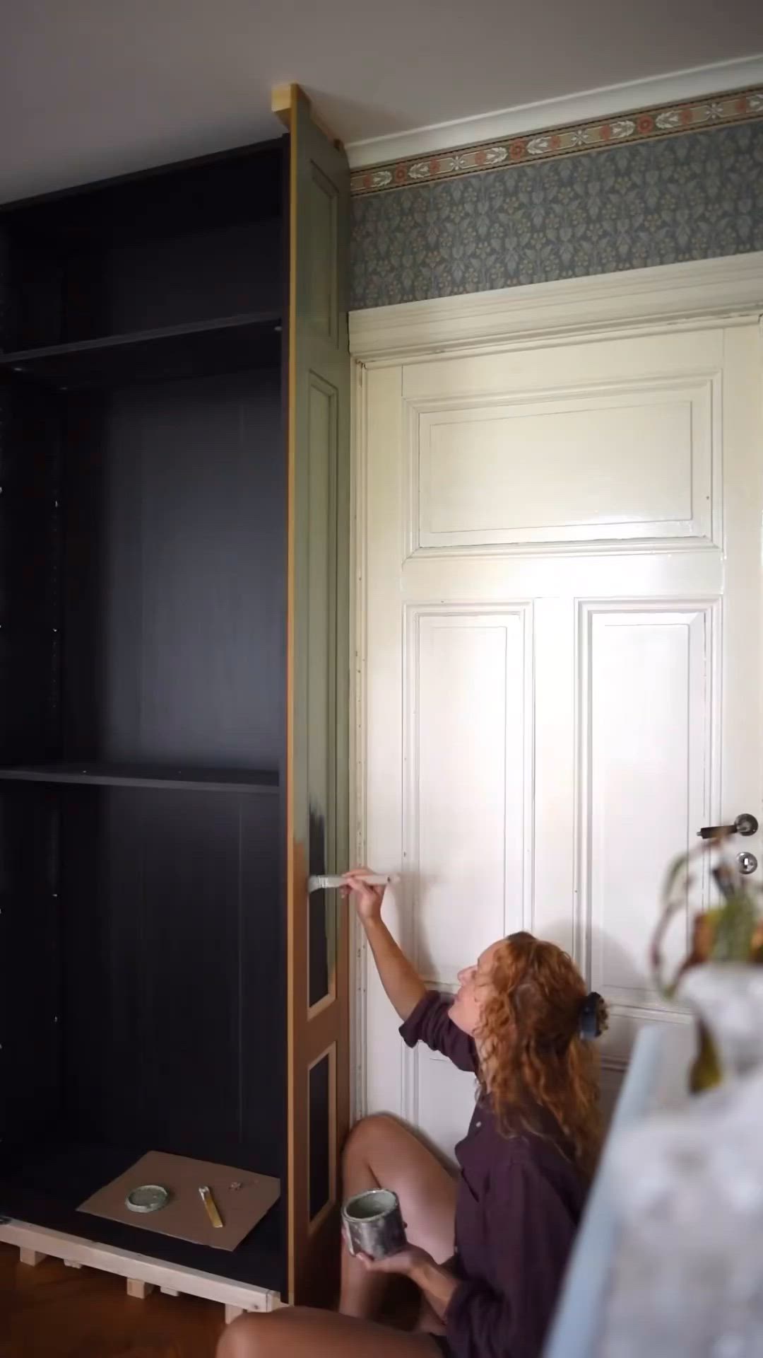 This may contain: a woman is painting the wall in her room with black paint and she has one hand on the door handle