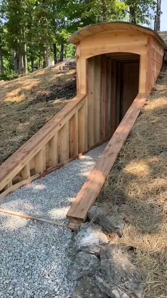 This may contain: a small wooden tunnel in the middle of a field next to some rocks and trees