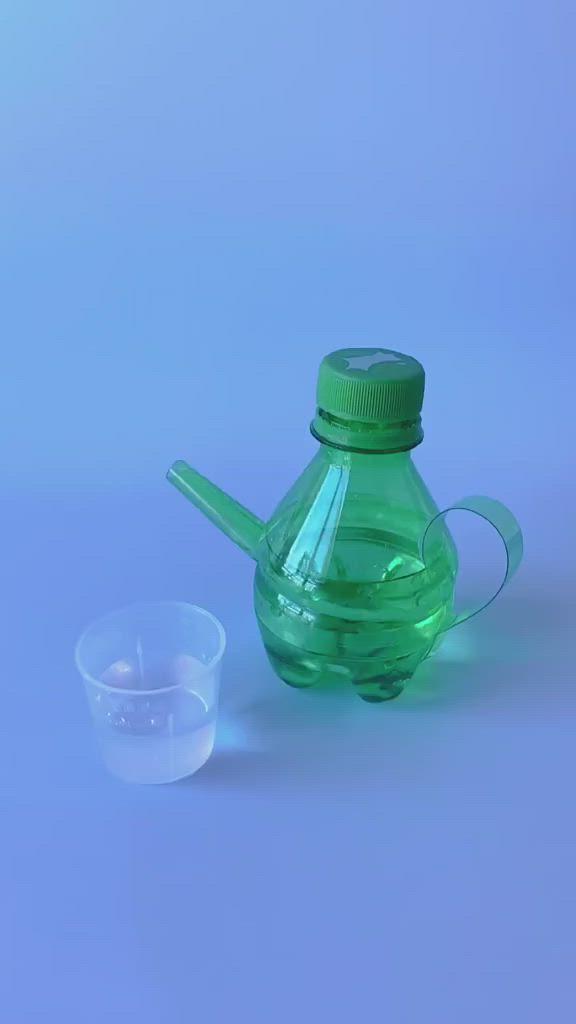 This may contain: a hand holding a green plastic bottle with a small cup in front of it on a blue background