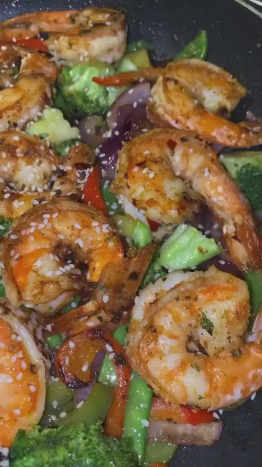 This may contain: shrimp, broccoli and peppers in a wok with sesame seeds on the side