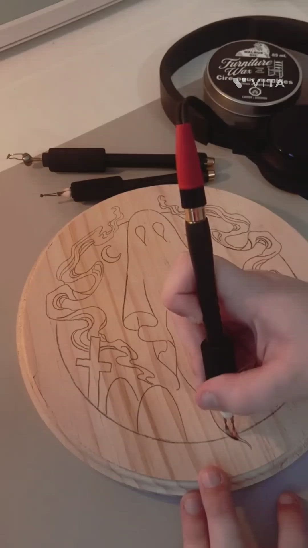 This may contain: a person holding a pen in their hand near a drawing on a wooden plate with scissors