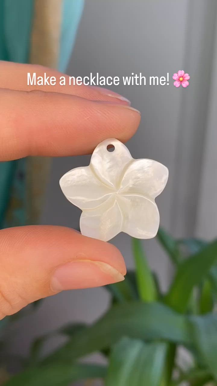 This may contain: a hand holding a white flower pendant in front of a potted plant