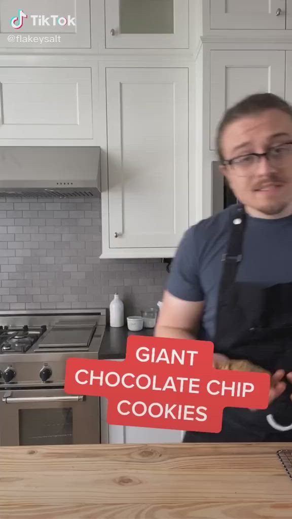 This may contain: a person holding a chocolate chip cookie in their left hand and cooling on a wire rack