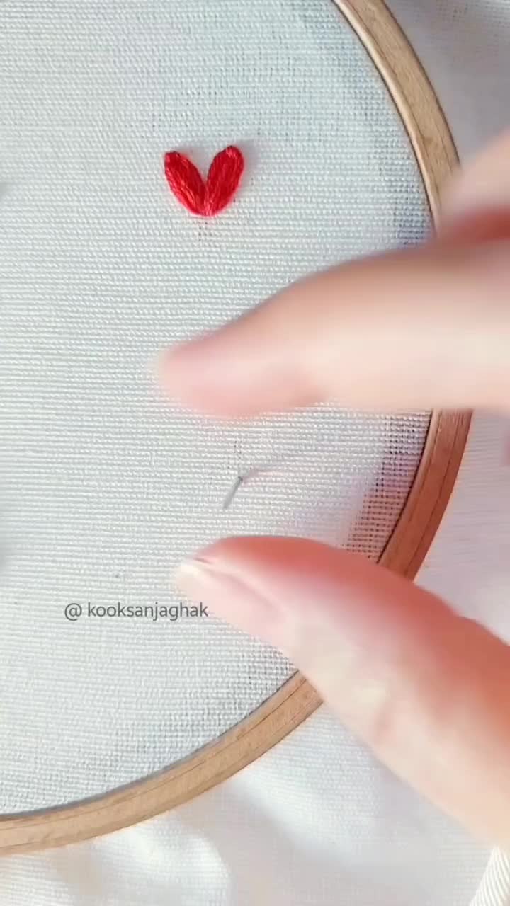 This may contain: someone is stitching a red heart on a white piece of fabric with a needle