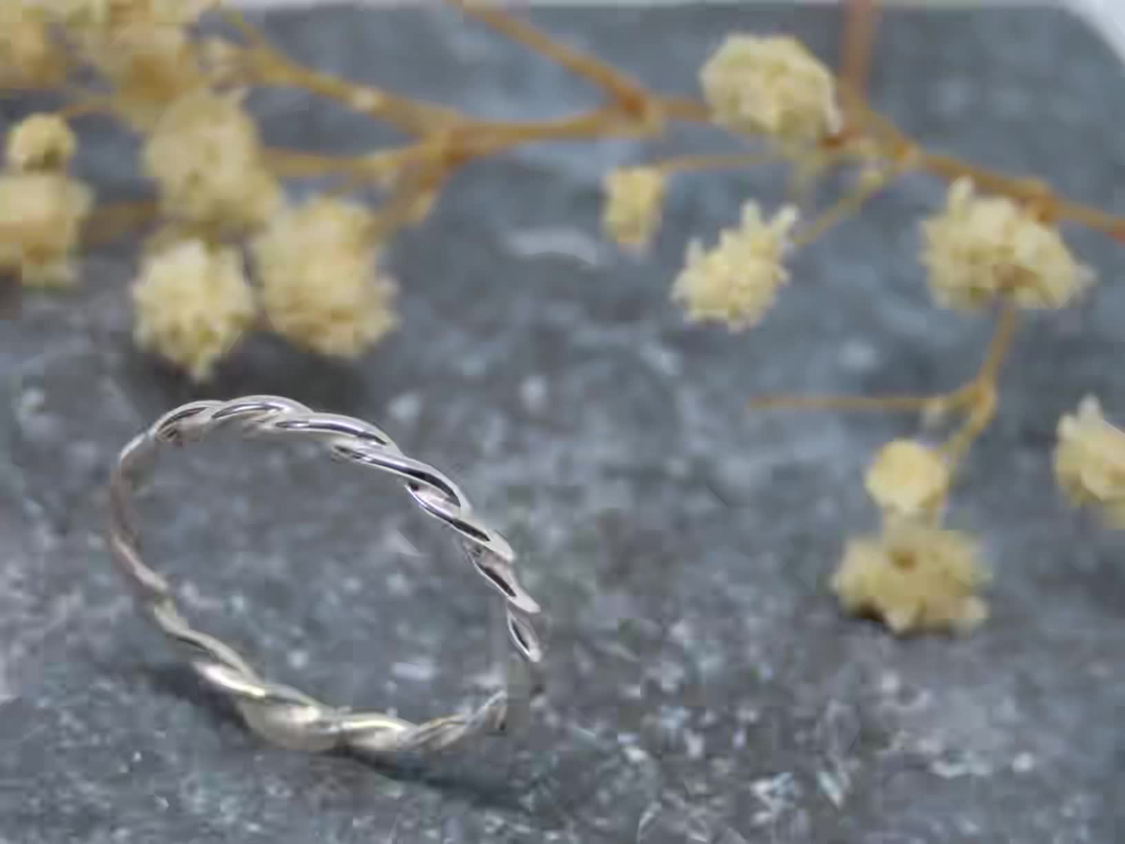 This may contain: a silver ring sitting on top of a rock next to some flowers and branches in the background