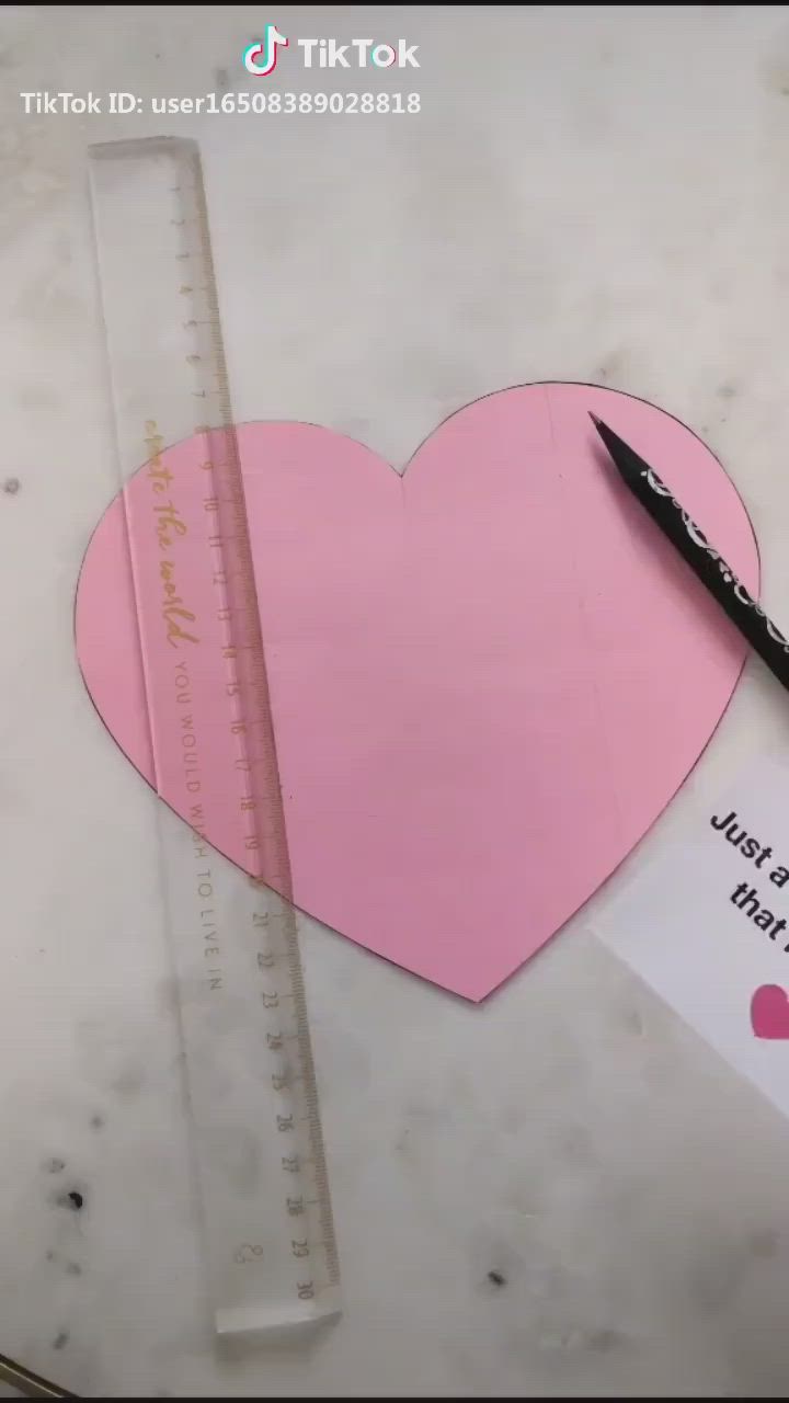 This may contain: a pink heart cut out from a piece of paper next to a pencil and ruler