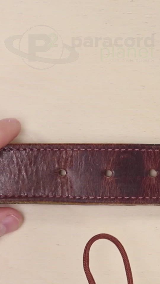 This may contain: a hand holding a brown leather belt with two holes in it and a string attached to the side