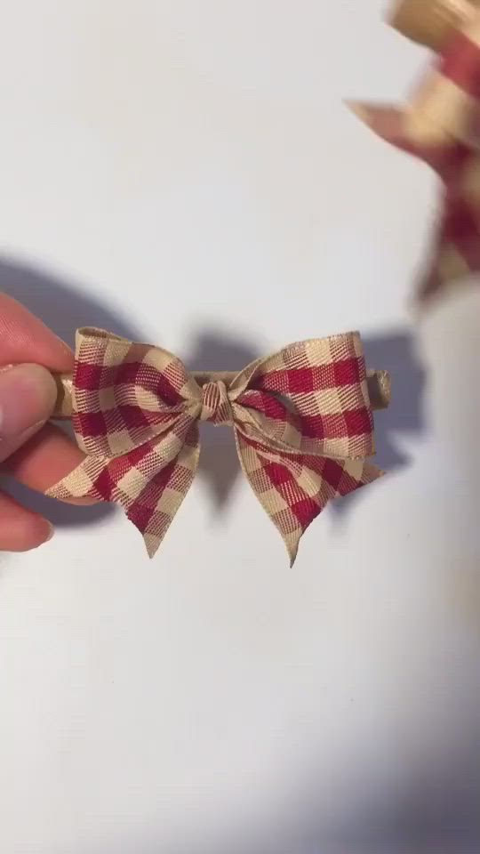 This may contain: a hand holding a bow that is attached to a string on a white surface with red and tan checkered fabric