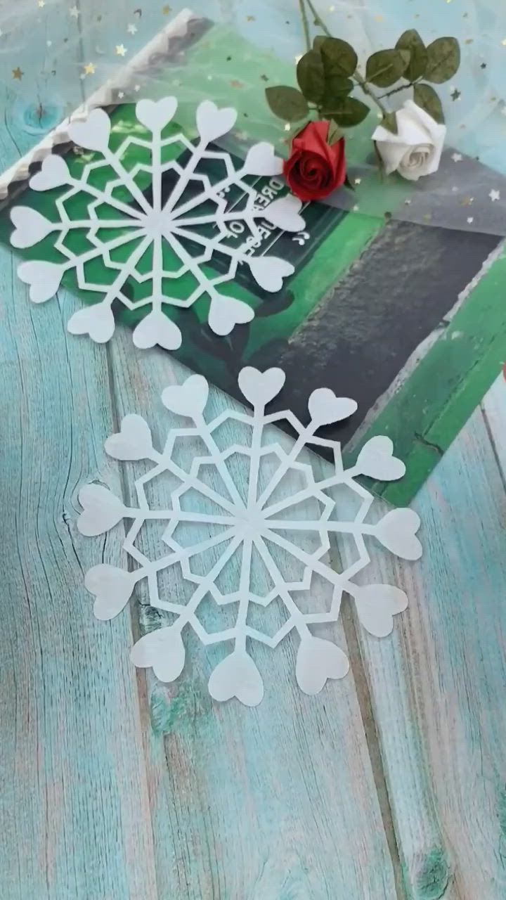 This may contain: some paper snowflakes sitting on top of a blue wooden table next to a red rose