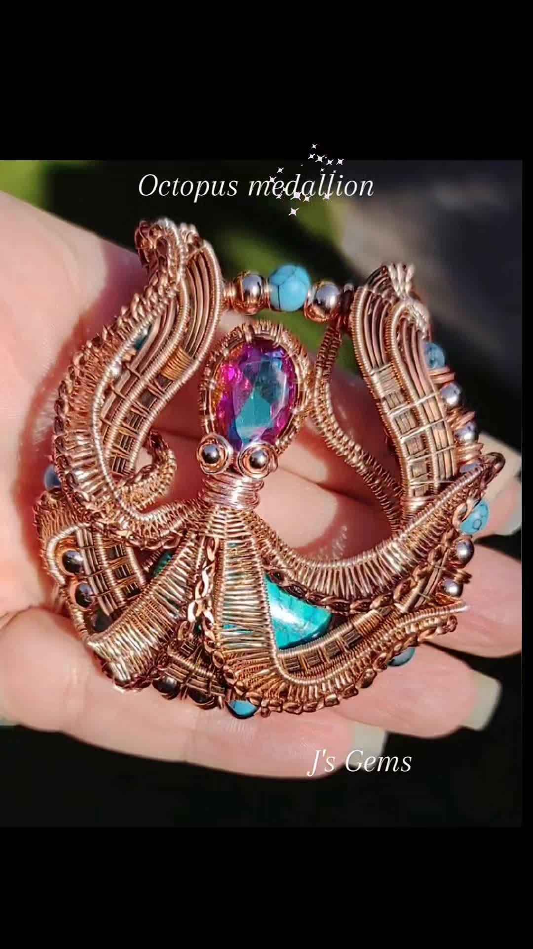 This may contain: a woman's hand holding a gold brooch with blue and pink stones on it