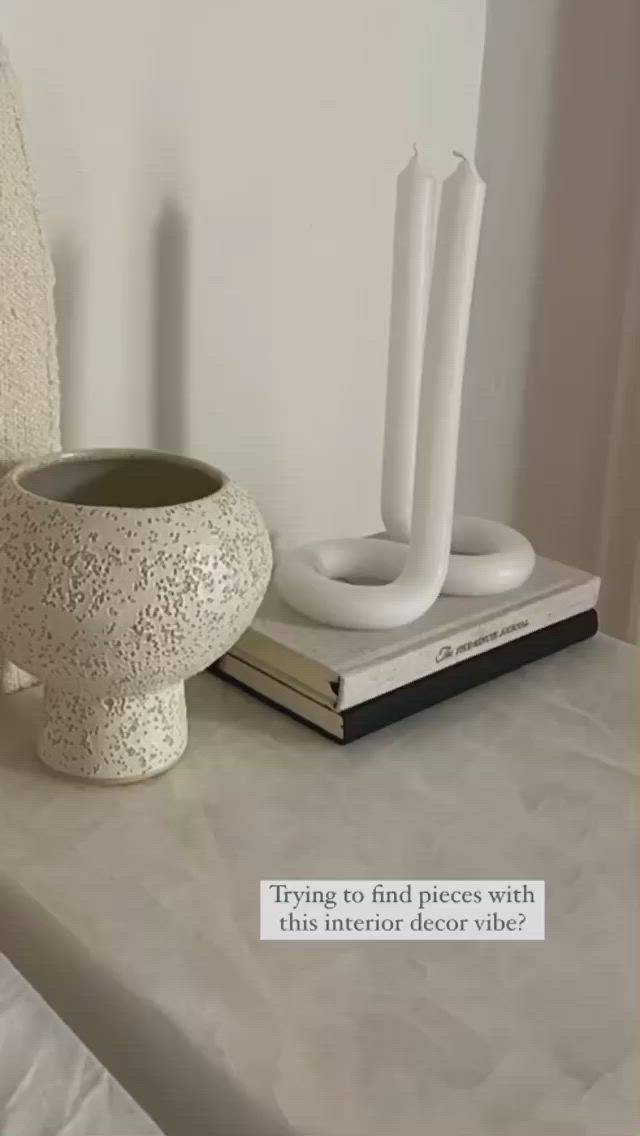 This may contain: a white vase sitting on top of a table next to a book and candle holder