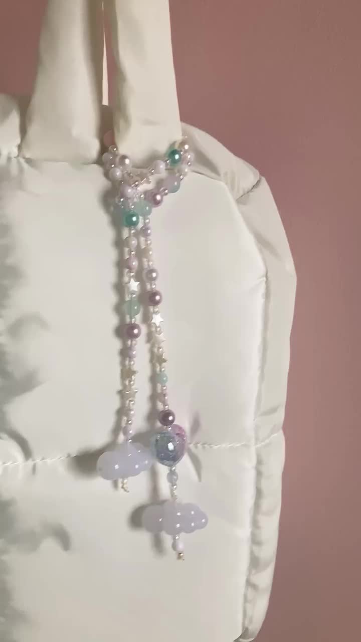 This may contain: a white bag with beads and charms hanging from it's side on a hanger