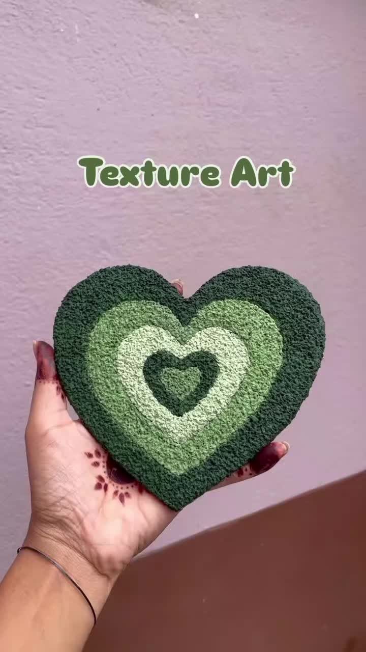 This may contain: a hand holding a green heart shaped rug with the words texture art written on it