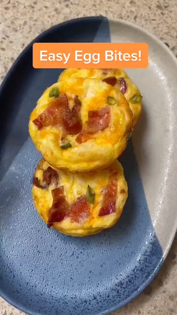 This may contain: an egg muffin with bacon and cheese on it being held by someone's hand