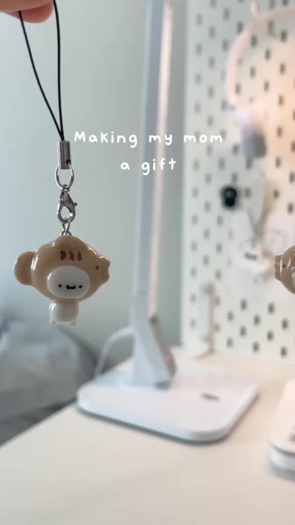 This may contain: a monkey keychain hanging from a cord next to a cell phone on a desk