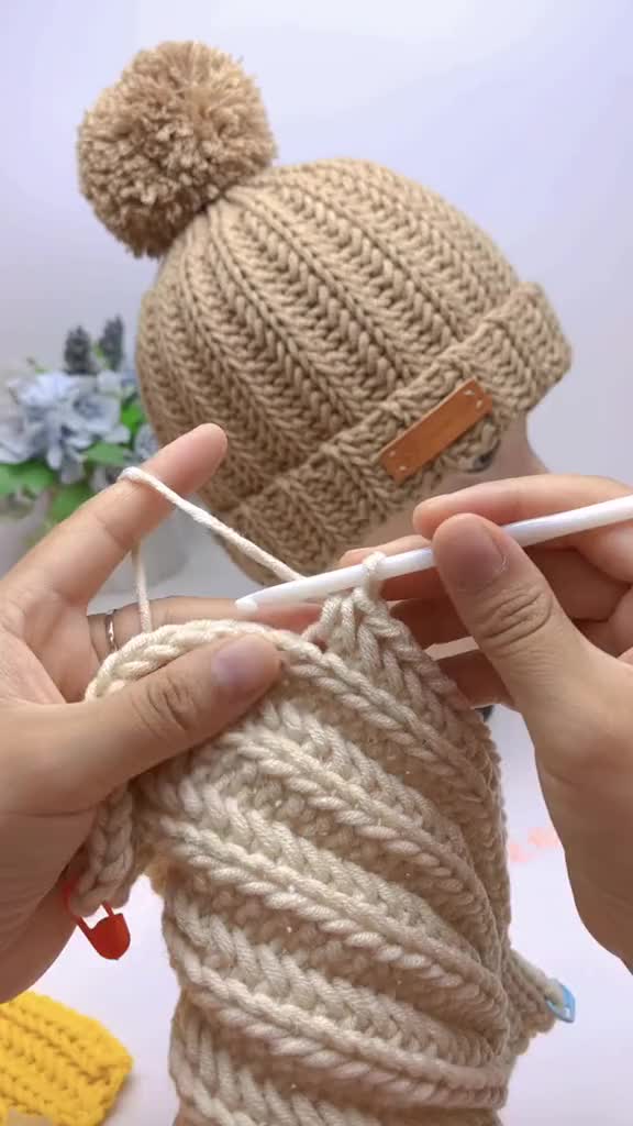 This may contain: two hands holding yarn and knitting needles in front of a knitted doll's head