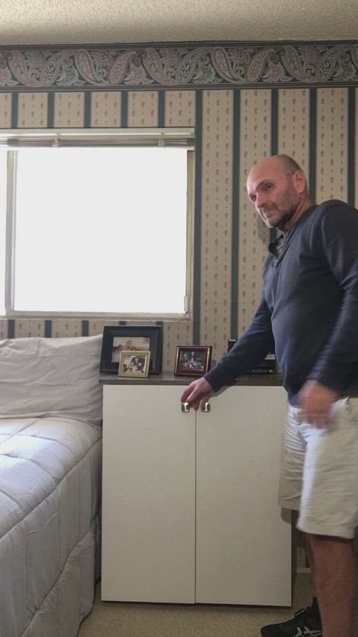 This may contain: a man standing next to a bed in a room with striped walls and clothes hanging on rails