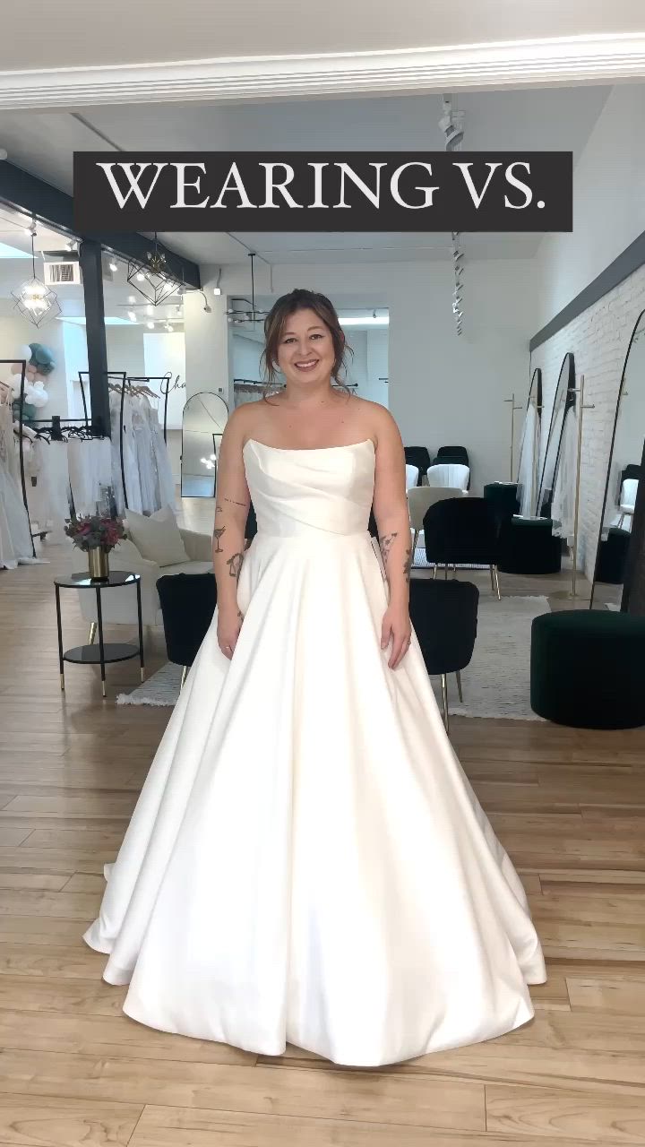 This contains: Bride in strapless ivory ballgown wedding dress showcasing a veil and jewelry.  The wedding dress has a scooped neckline with points and ruching and the full ballgown skirt has pockets.