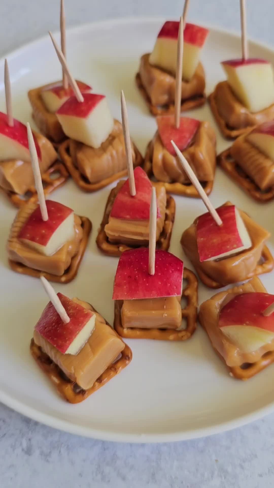 This may contain: caramel apple pretzel bites on a plate with toothpicks sticking out