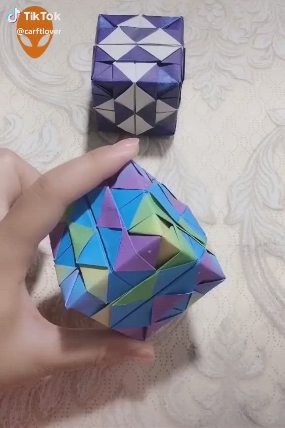 This may contain: the hand is holding an origami cube in one hand and another on the other