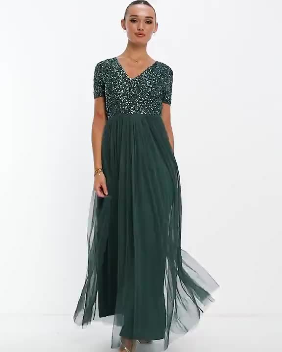 This may contain: a woman in a long green dress with sequins on the neck and sleeves