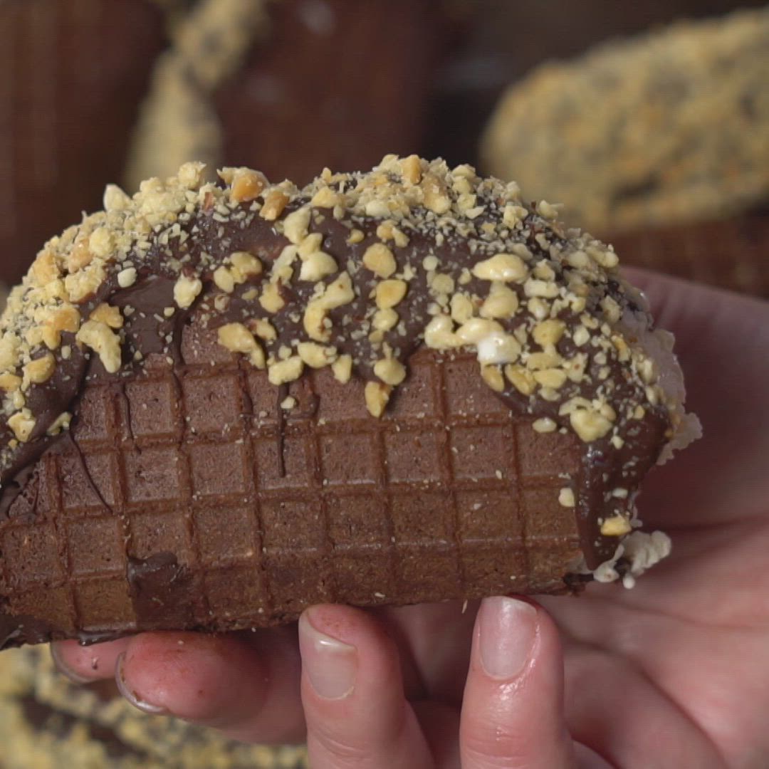 This may contain: a person holding up a chocolate donut with nuts on it's side and sprinkled in chocolate