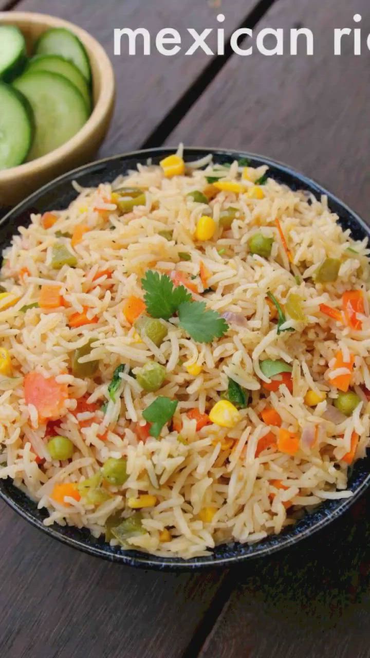 This may contain: mexican rice with carrots, peas and cucumbers in a black bowl on a wooden table