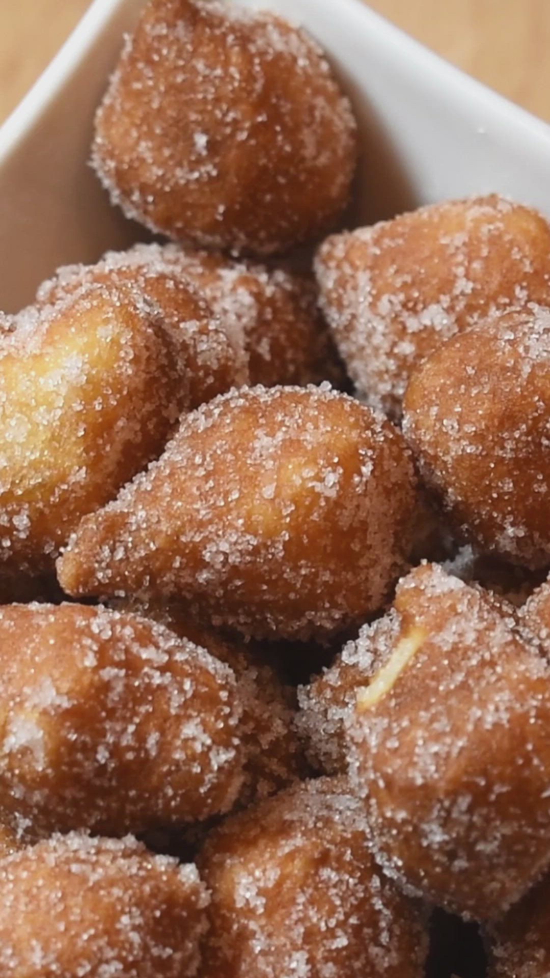 This may contain: a bowl filled with sugar covered doughnuts on top of a wooden table and the words ingredient donuts above it