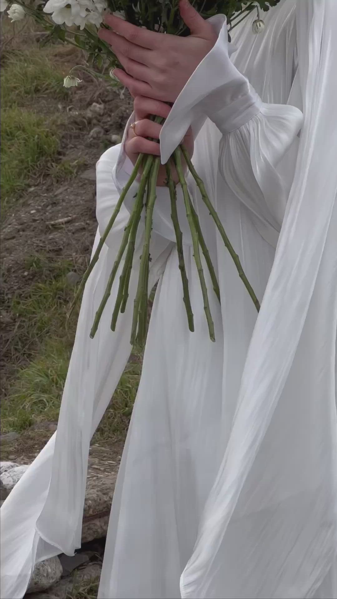 This may contain: a woman in a white dress holding a bouquet of daisies on her wedding day