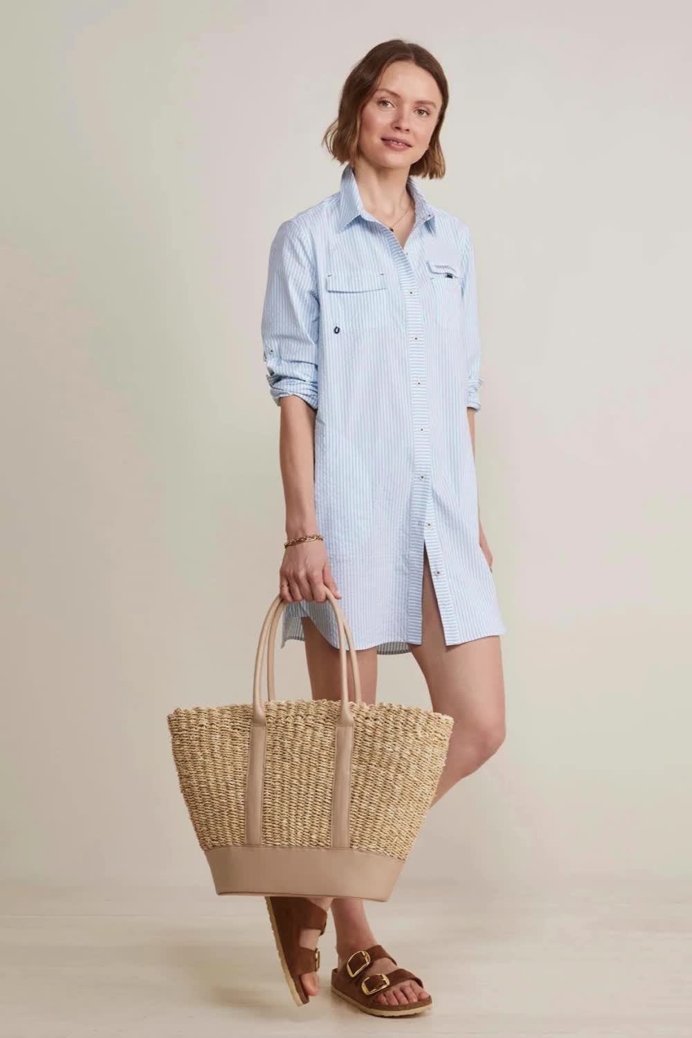 This contains: A person standing in front of a beige background wearing a blue and white striped shirt dress