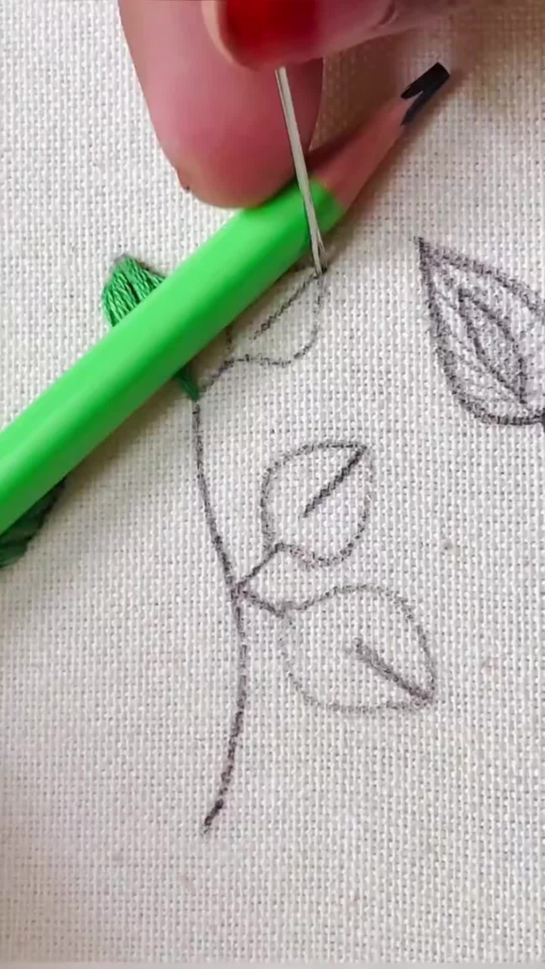 This may contain: someone is stitching leaves on a piece of fabric with a green crochet hook