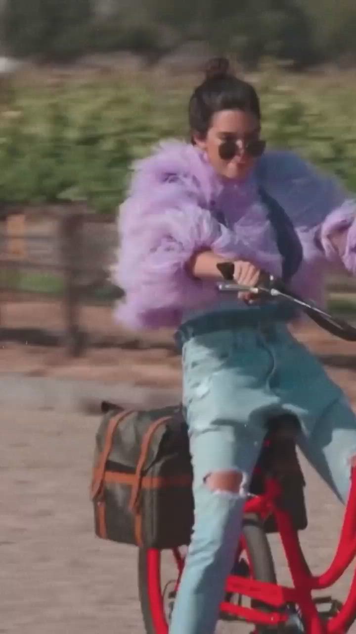 This may contain: a woman riding on the back of a red bike with pink fur coat over her shoulders