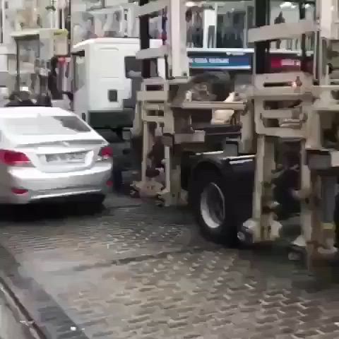 This may contain: a white car driving down a street next to a truck with crates on it's back