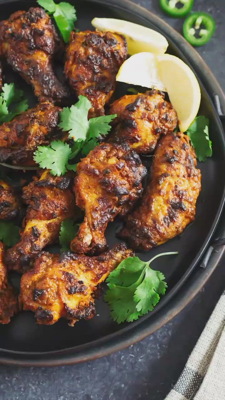 This may contain: chicken wings with cilantro, lemon and parsley on a black platter