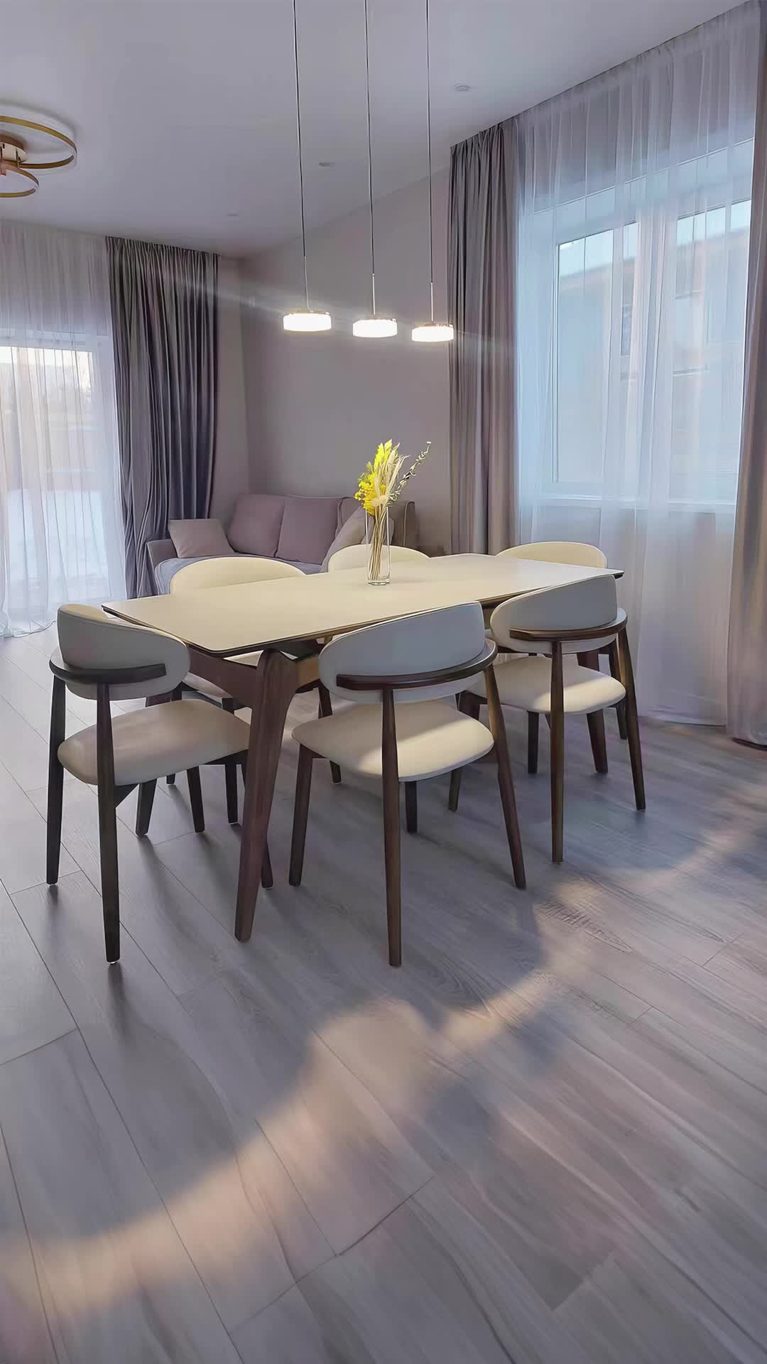 This contains: Promotional image for Benenden Dining Chairs from Brightly Home, featuring a minimalist styled dining room with linen and leather chairs around a white table, complemented by subtle drapery and pendant lighting.