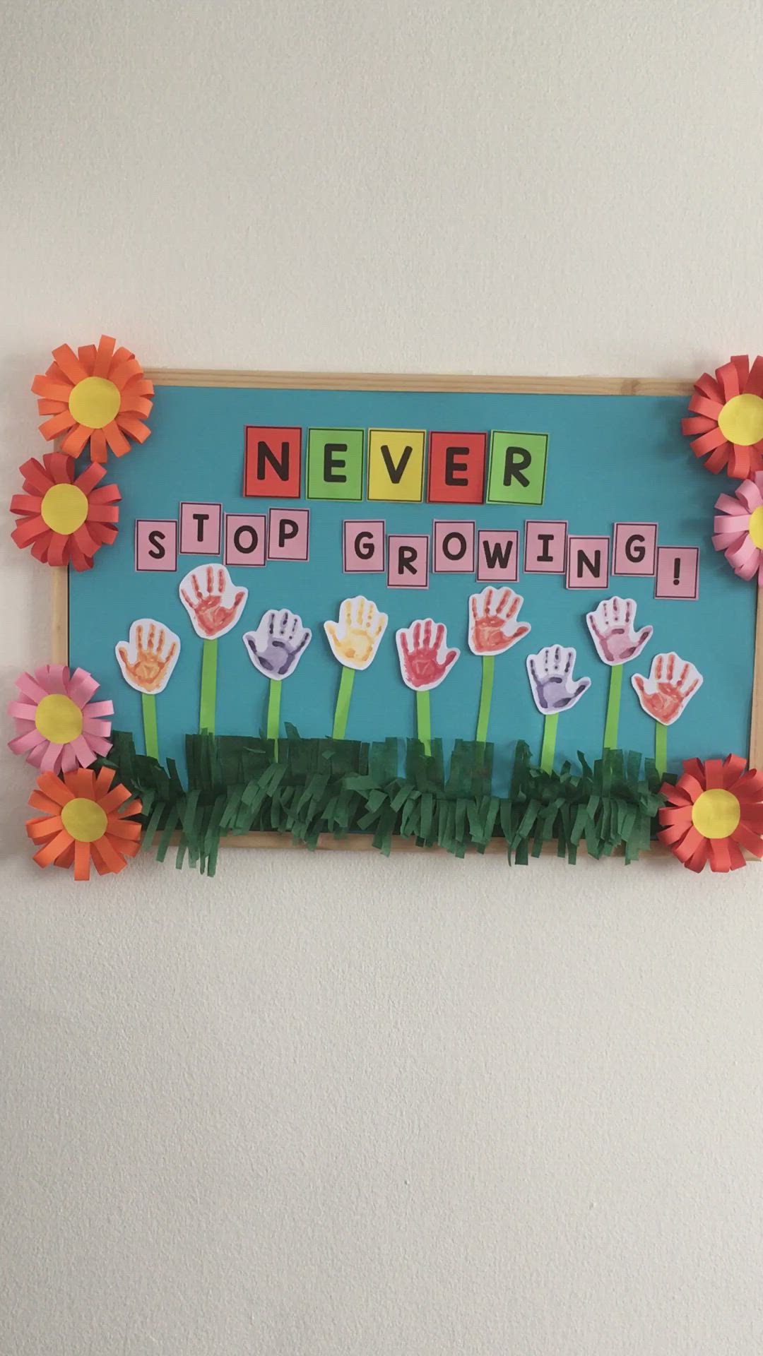 This may contain: a sign that says never stop growing with flowers and handprints on the letters