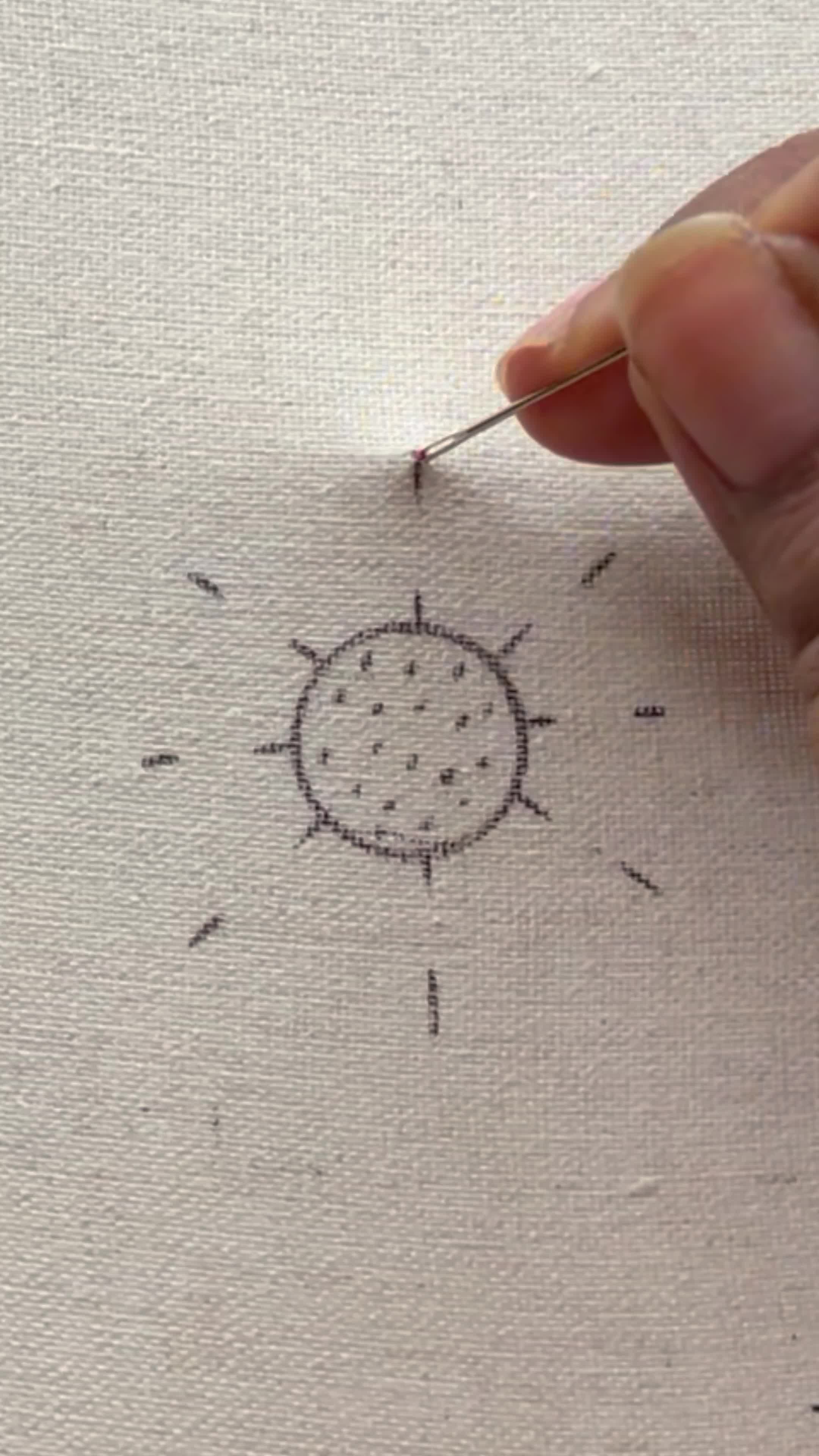 This may contain: someone is stitching something on the fabric with pink thread and needles to make an embroidered sunburst