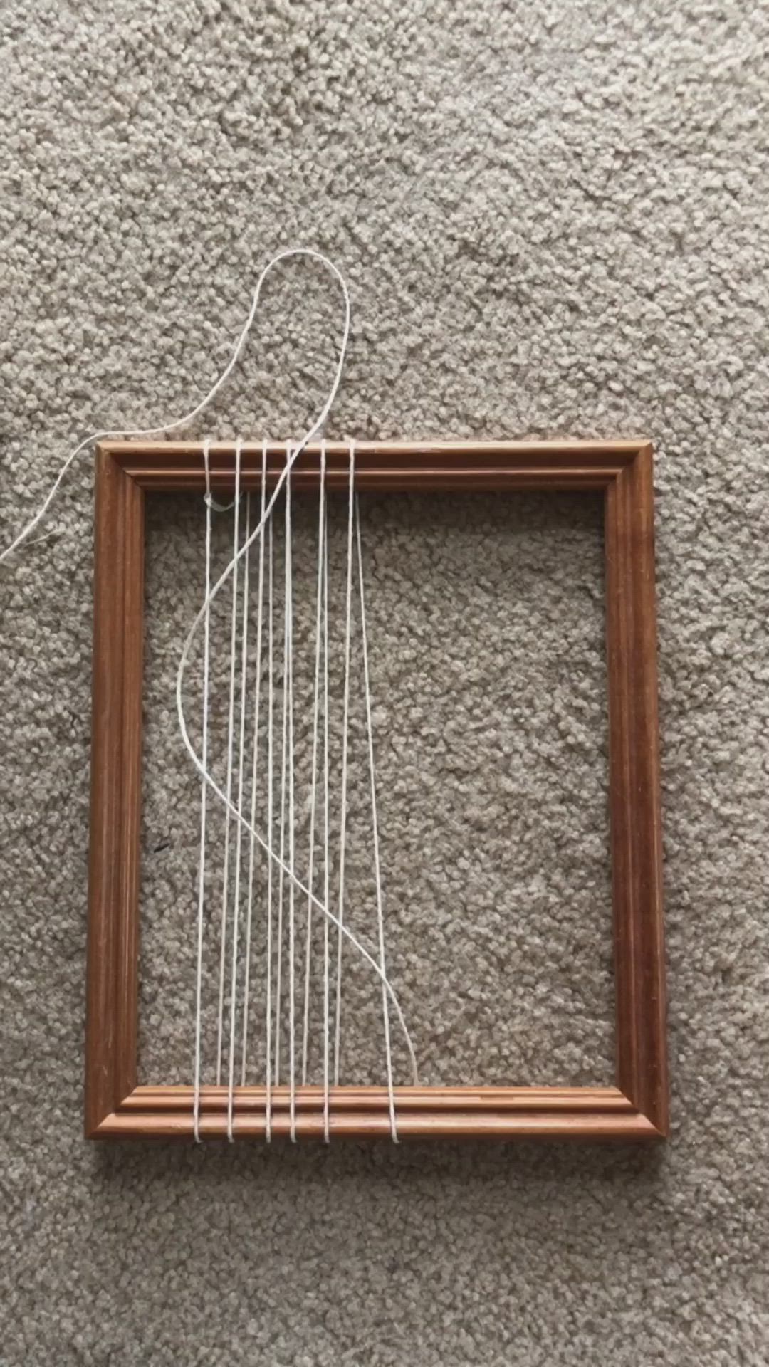 This may contain: a square frame with some white thread in it on the ground next to a wall