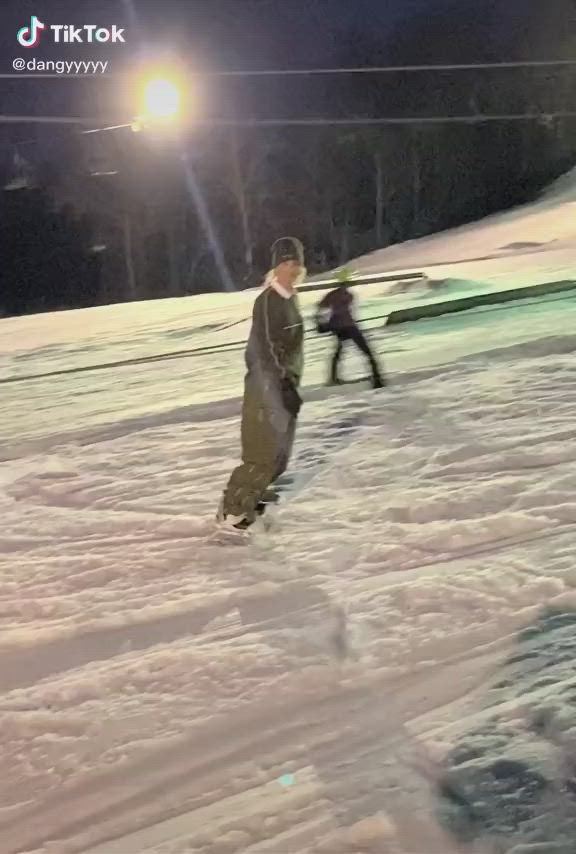 This may contain: two snowboarders going down a snowy hill at night