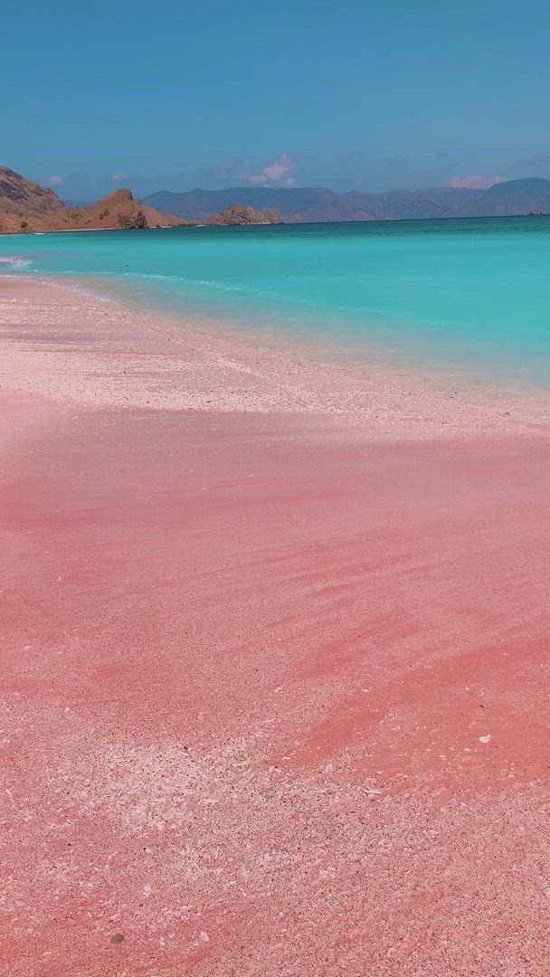 This may contain: pink sand and water on the beach with mountains in the background